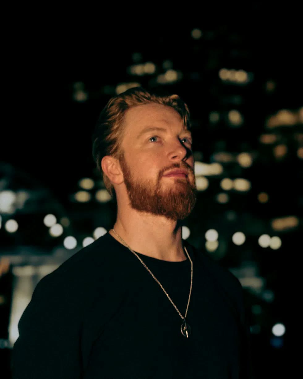 Kyle Redstone looking up into warm light, with blurred city lights behind him at night