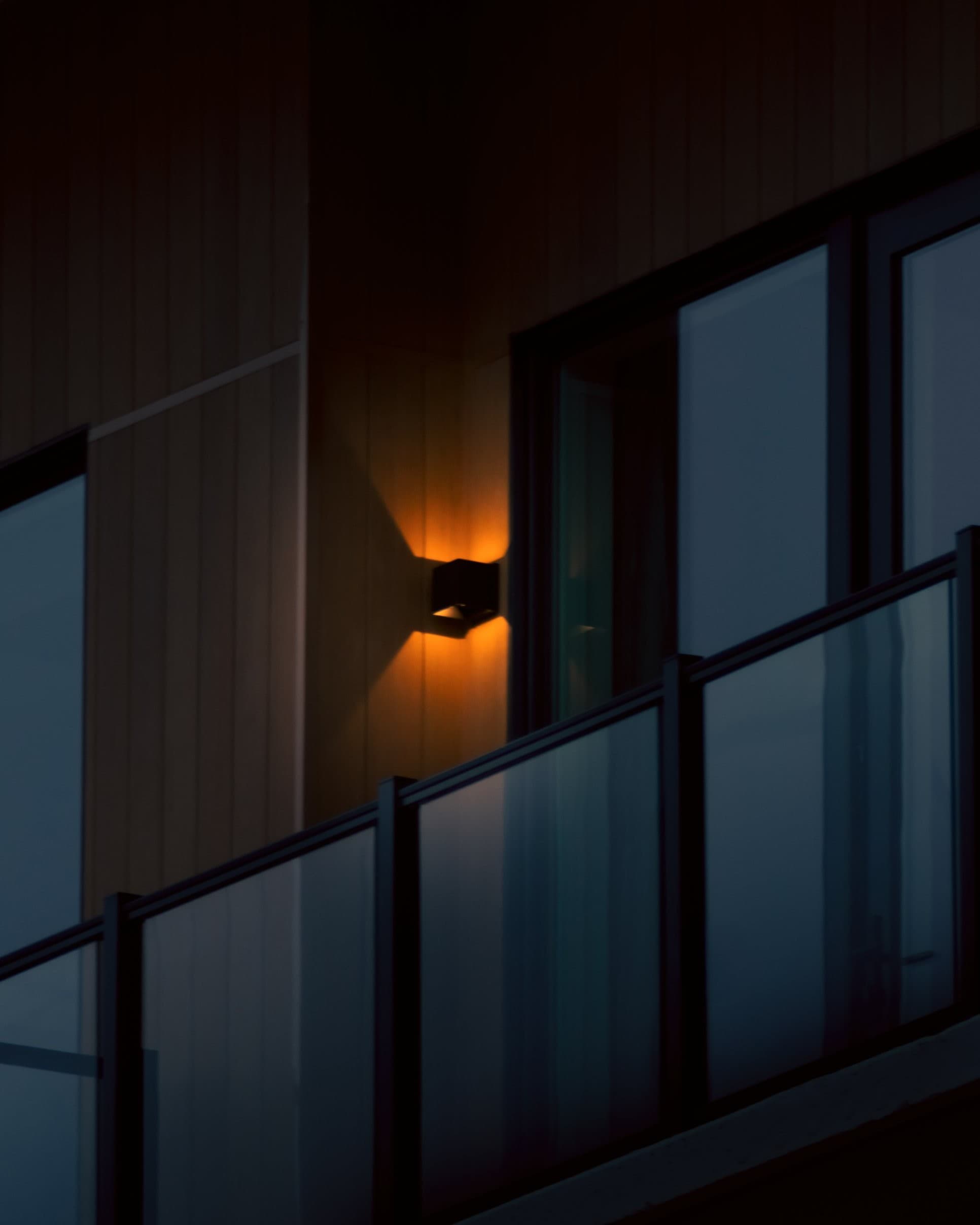 A single orange wall sconce glowing against dark blue glass balconies at twilight