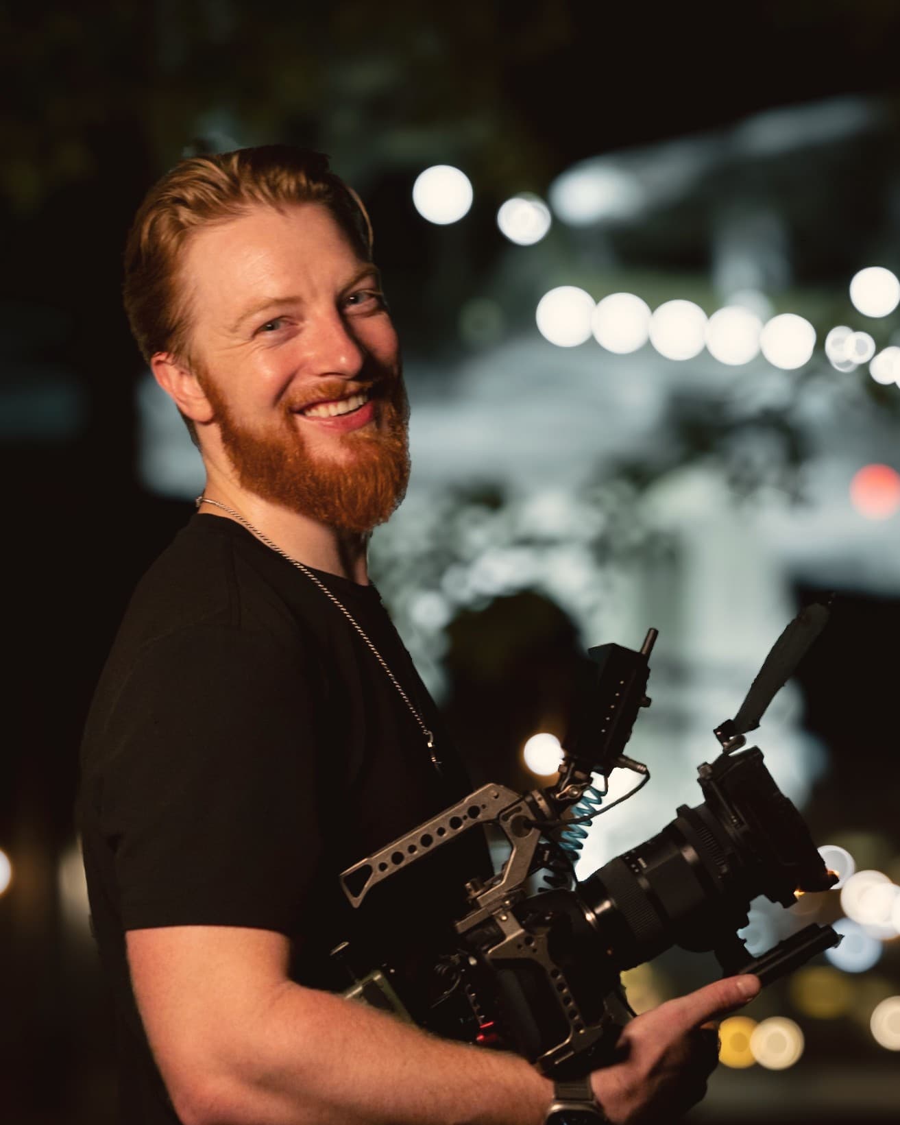 Kyle Redstone smiling, holding a cinema camera rig on a night street
