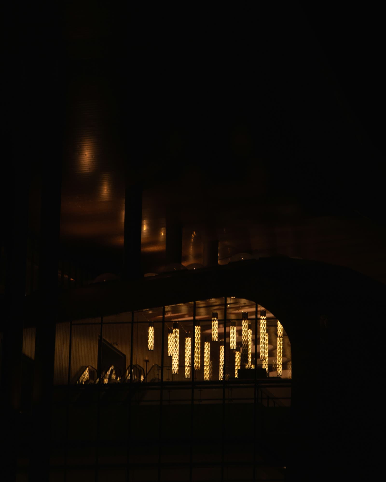 Warm pendant lights glowing through a glass wall into a dark building at night