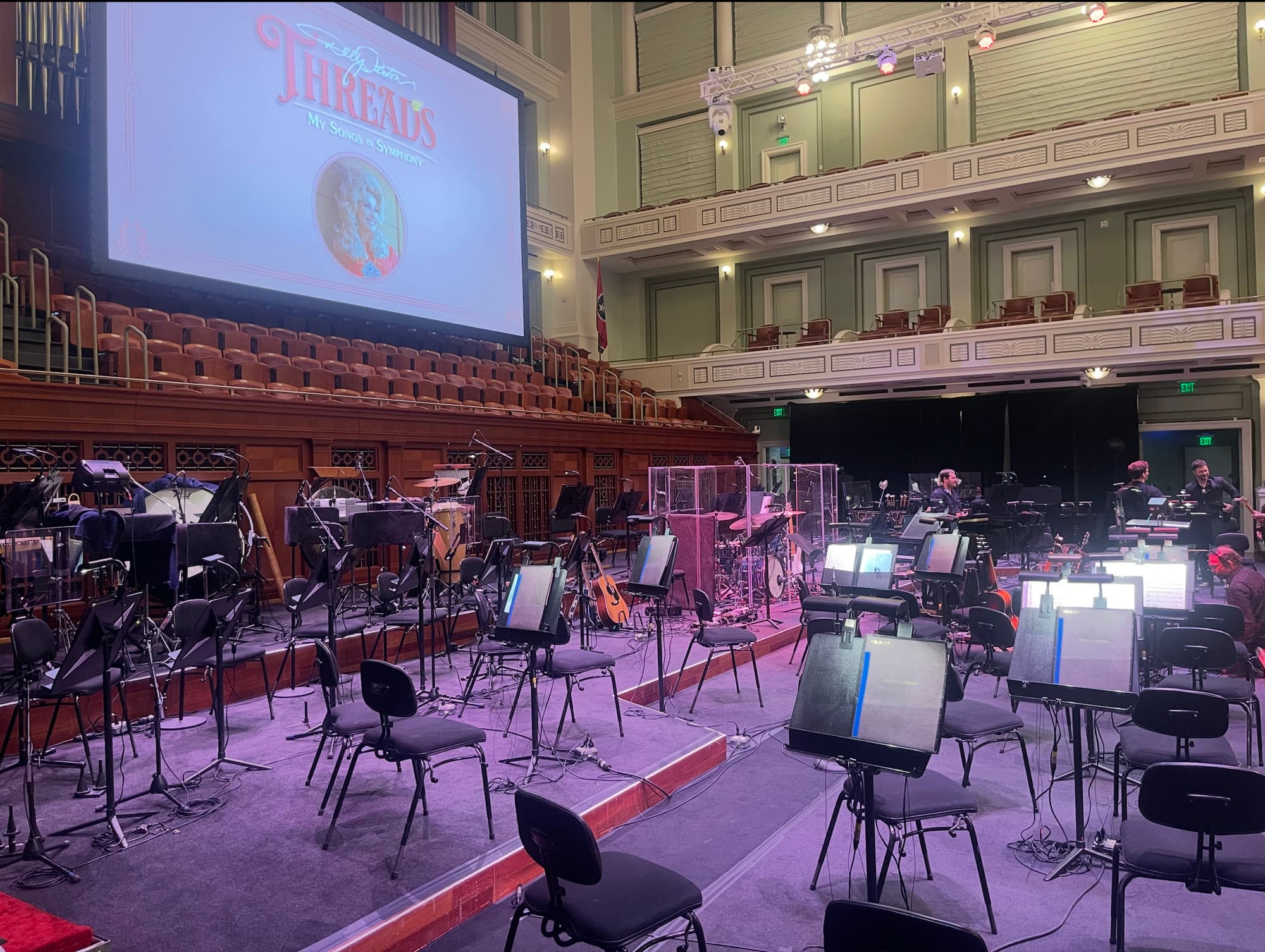 The Schermerhorn stage set for Threads before the concert: empty chairs and lit music stands, the drum kit behind clear shields, and the Threads title on the big screen