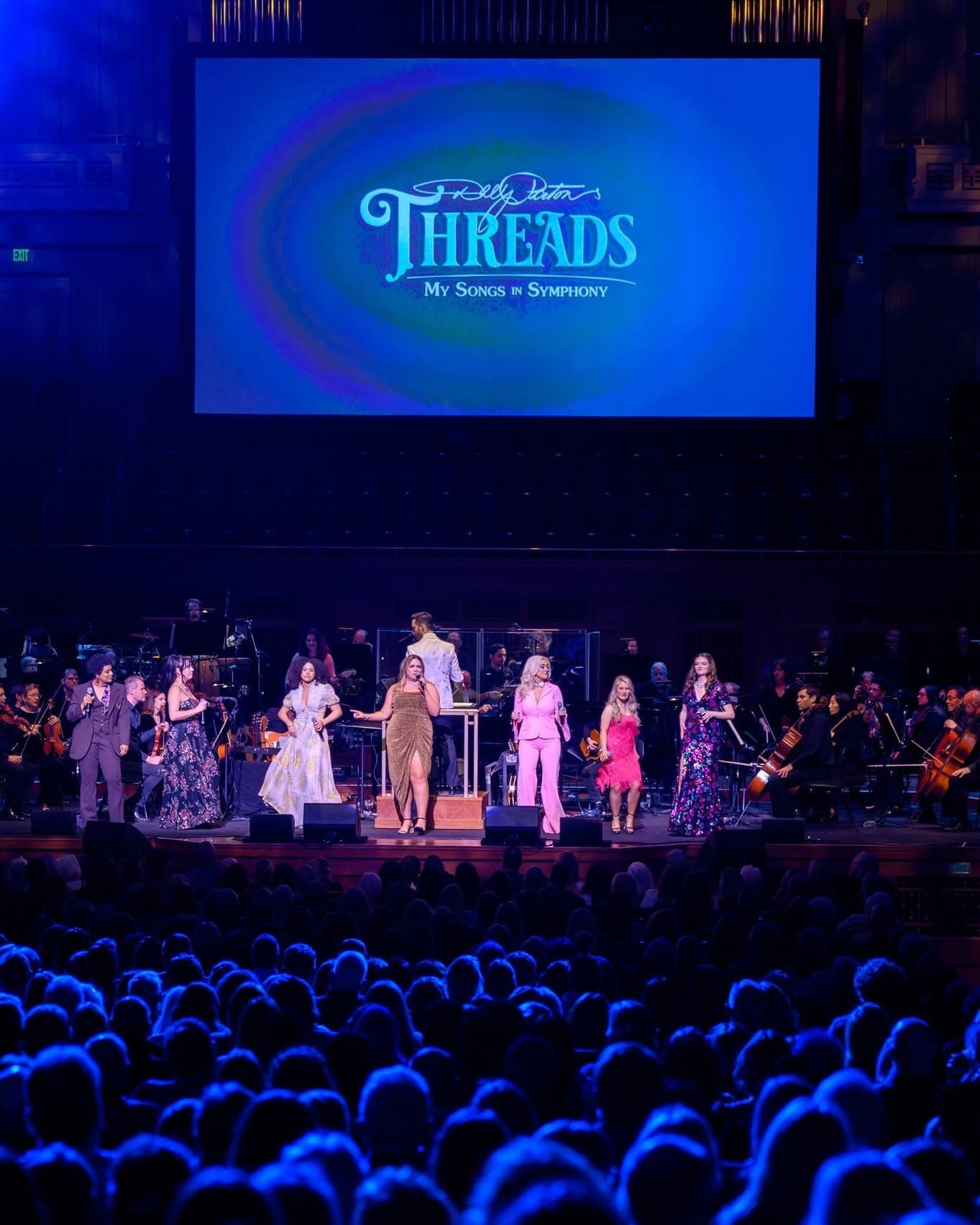 The Threads title screen above the orchestra and seven singers, with a full house in the foreground